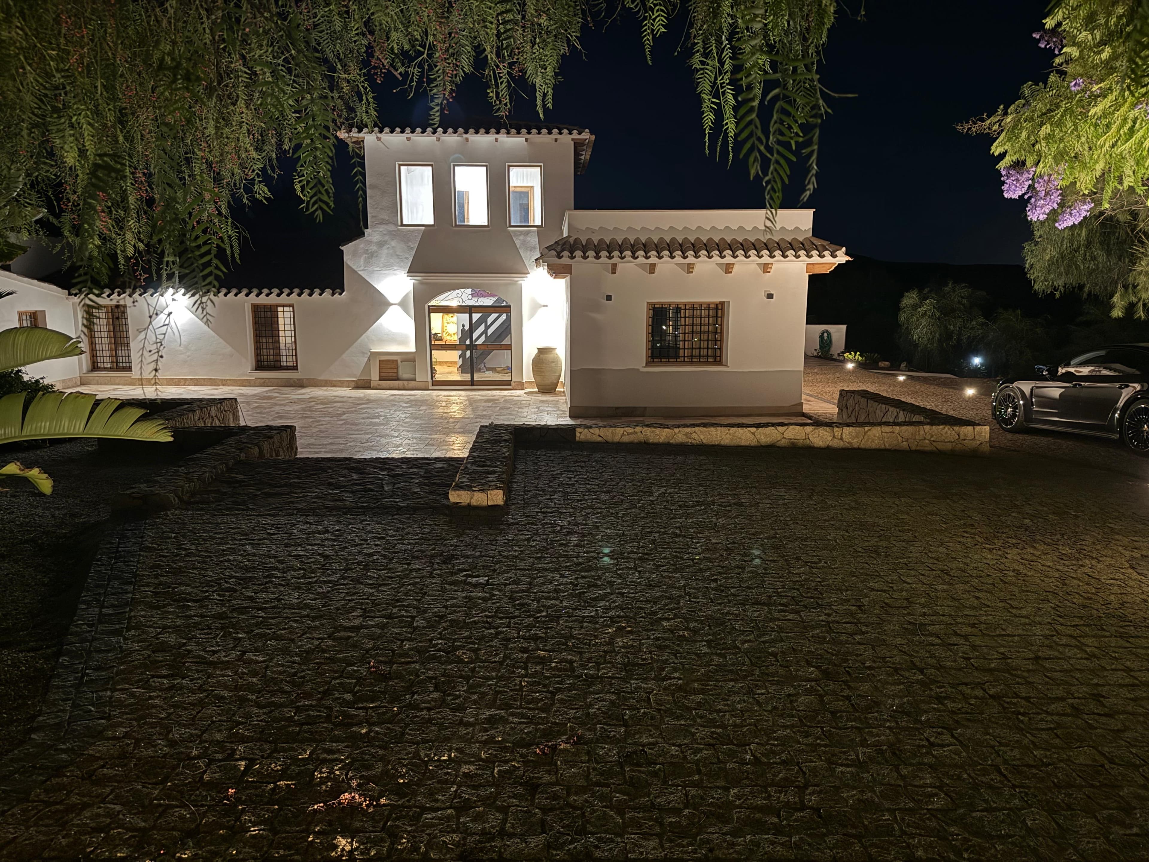 La misma fachada de noche, con las ventanas y los muros iluminados