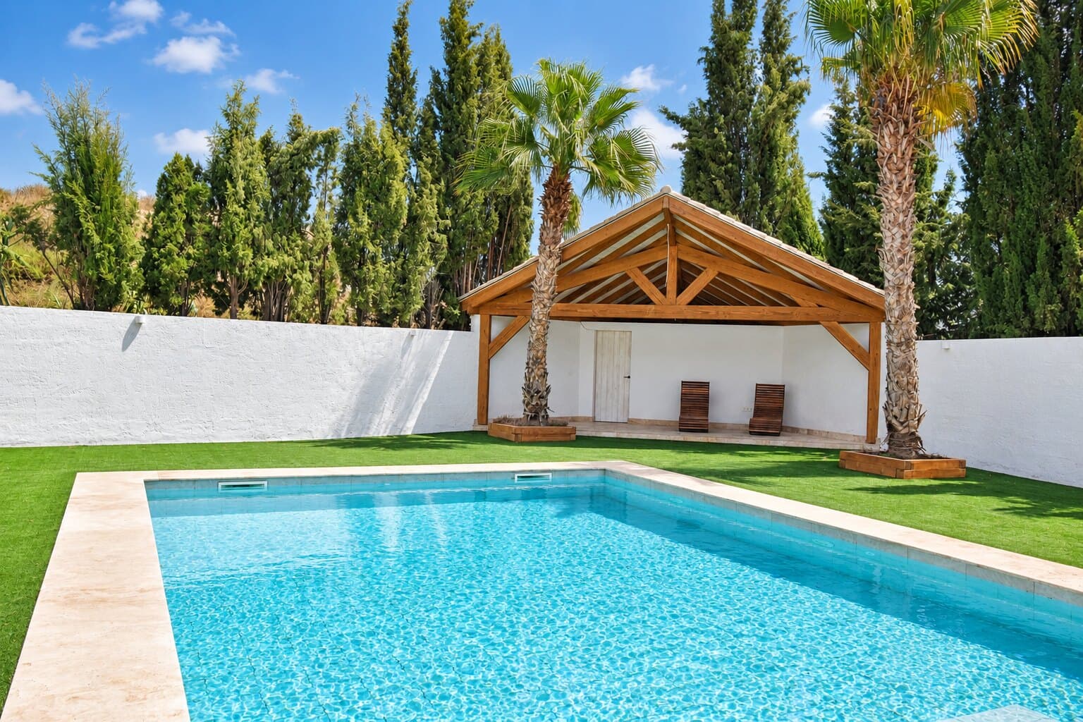 Piscina privada entre césped, palmeras y cipreses
